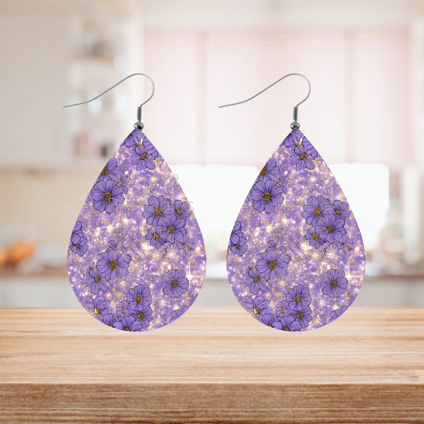 Teardrop earrings with purple flowers and gold glitter on a wooden surface.