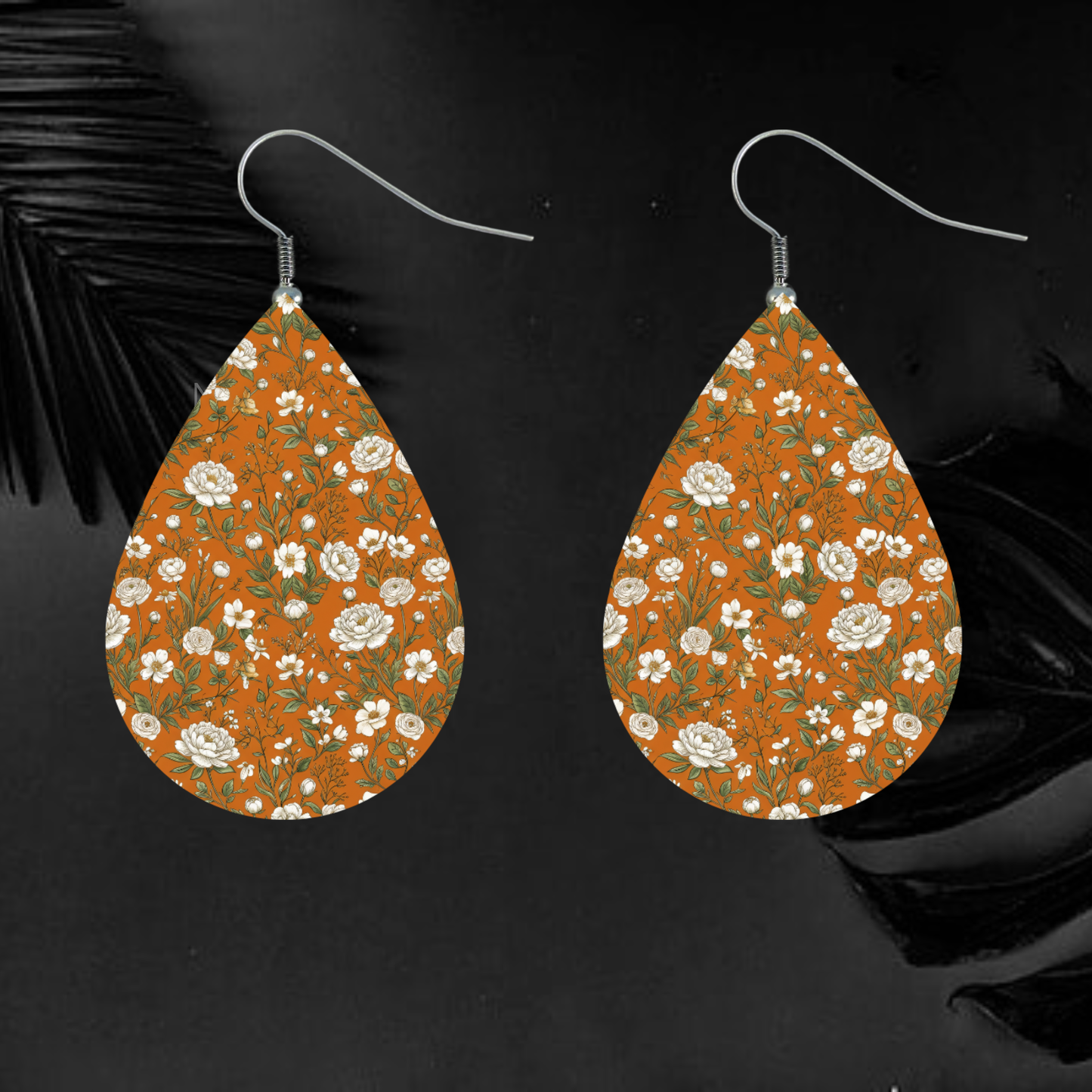 Teardrop earrings with an orange floral pattern and silver hooks on a dark background.
