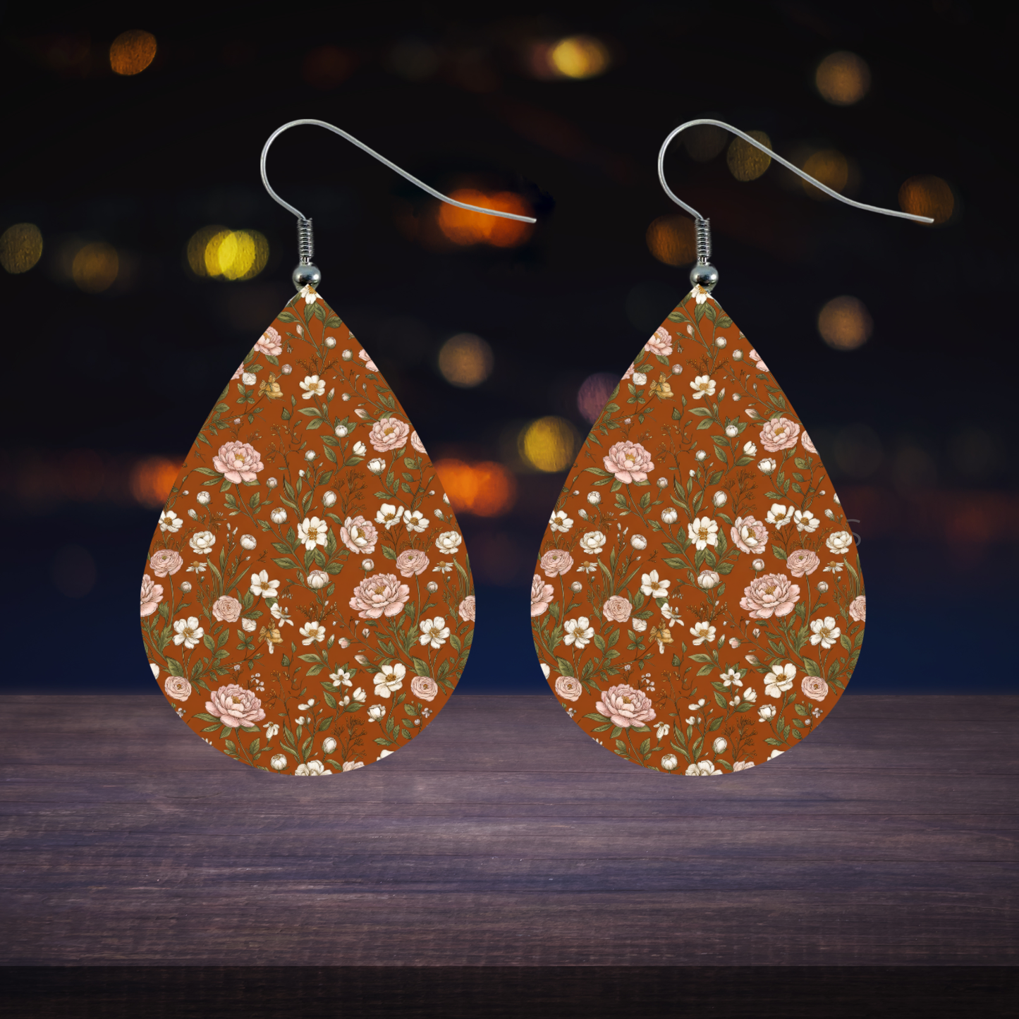 Teardrop earrings with floral pattern on brown background and bokeh lights.