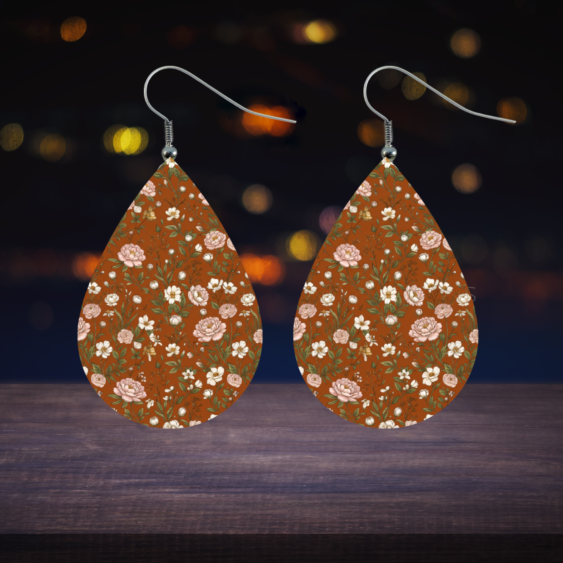 Teardrop earrings with floral pattern on brown background and bokeh lights.