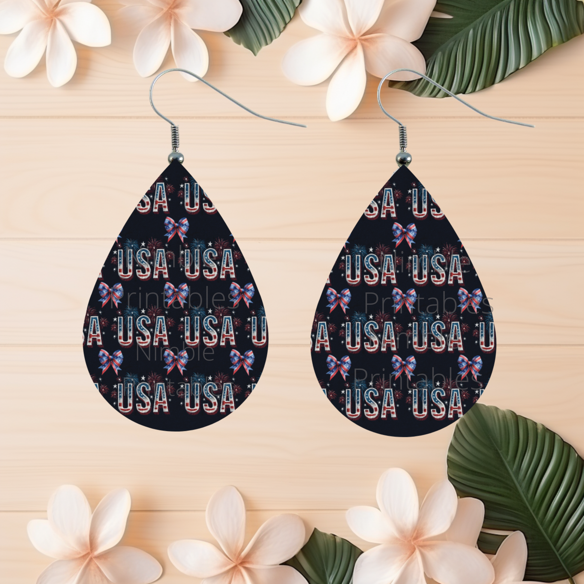 Teardrop earrings with repeating "USA" text and bows, set against a wooden background.