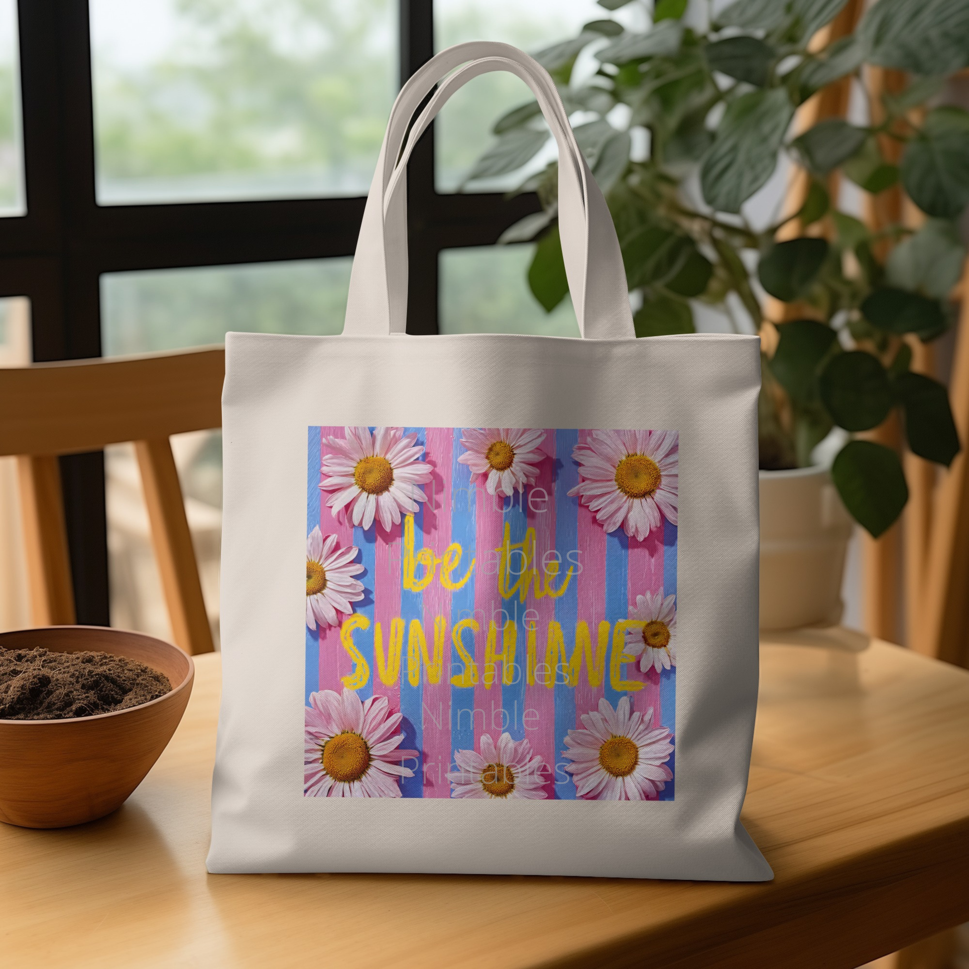 White tote bag with "Be the sunshine" text and daisies on striped background.